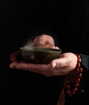 adult man in a black shirt rotates a wooden stick around a copper Tibetan bowl of water. ritual of meditation, prayers and immersion in a trance. Alternative treatment