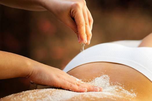 Close up detail of therapist applying salt on female back. Woman having therapeutic halo therapy in spa.