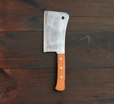 large kitchen knife for cutting meat and vegetables on a brown wooden background, top view