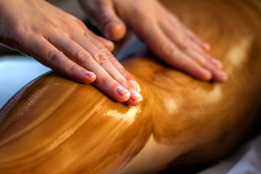 Close up detail of hands massaging female calf muscle with hot chocolate oil.
