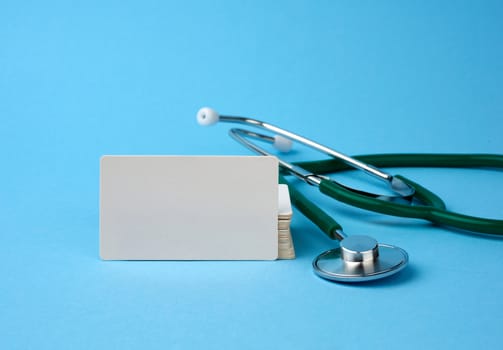 medical stethoscope and empty paper business cards on a blue background, selective focus 