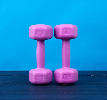 pink plastic dumbbells of one kilogram on a blue background, sports equipment