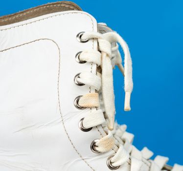 fragment of white leather figure skates with white textile laces on a blue background