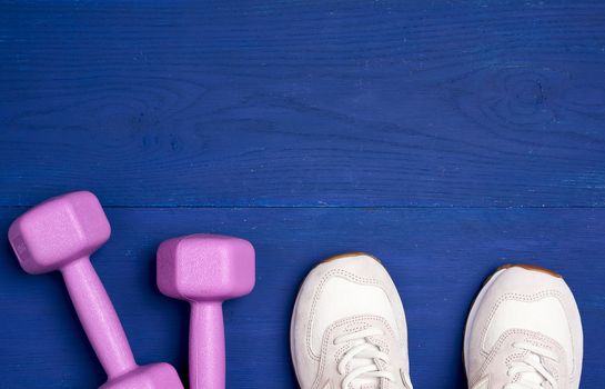 pink plastic dumbbells of one kilogram and white sport shoe on a blue background, sports equipment, top view