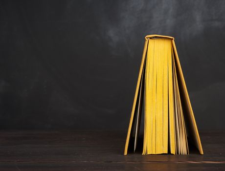 open book in yellow hardcover against a black chalk board, copy space