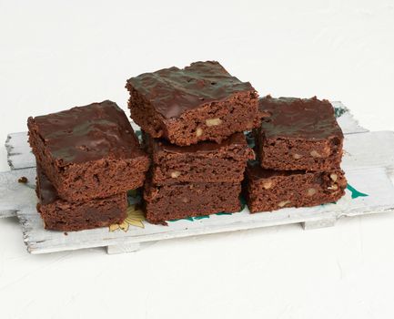 stack of square baked slices of brownie chocolate cake with walnuts on a wooden board, top view