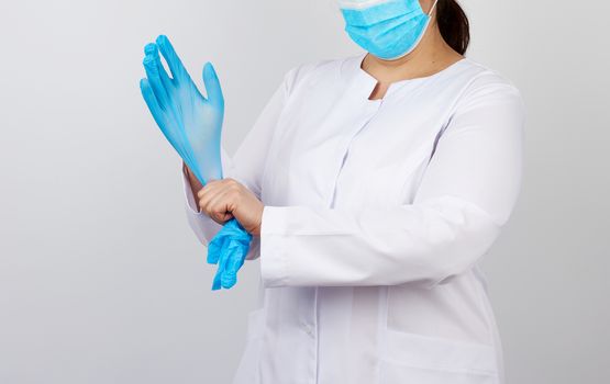 medical doctor in a white coat and mask puts on medical hands latex gloves before procedures, white studio background, copy space