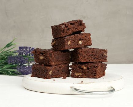stack of square baked slices of brownie chocolate cake with walnuts on a round white wooden board
