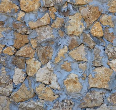 wall of yellow stones of different sizes fastened with gray cement, full frame