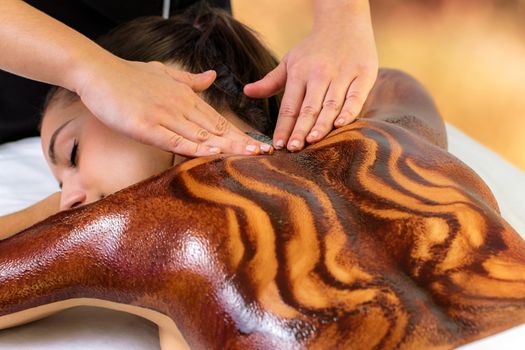 Close up of woman having hot antioxidants chocolate back massage. Beautician rubbing dark cacao wax on skin.