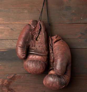 pair of brown leather boxing gloves hang on a wooden wall, sports equipment