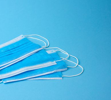 stack of white medical textile individual masks with elastic bands for protection against virus and bacteria on a blue background, copy space