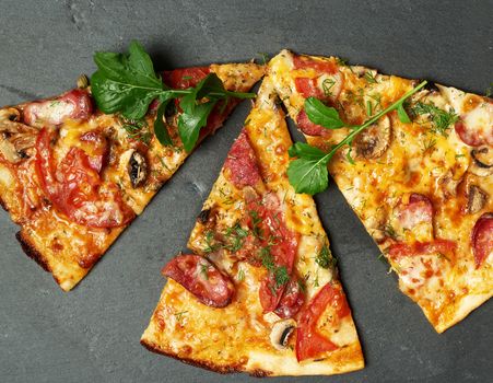 baked round pizza with smoked sausages, mushrooms, tomatoes, cheese and arugula leaves, food is cut in portions, full frame