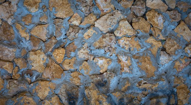 wall of yellow stones of different sizes fastened with gray cement, full frame