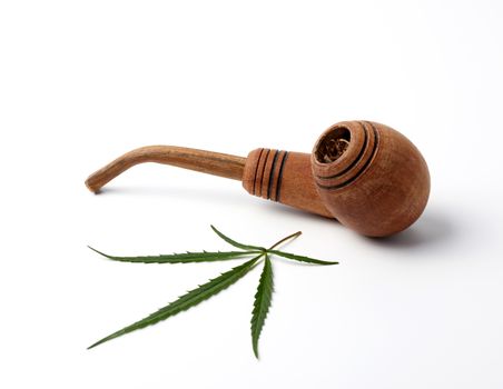 wooden smoking pipe and green hemp leaves on a white background, concept of legalization of marijuana for alternative medicine