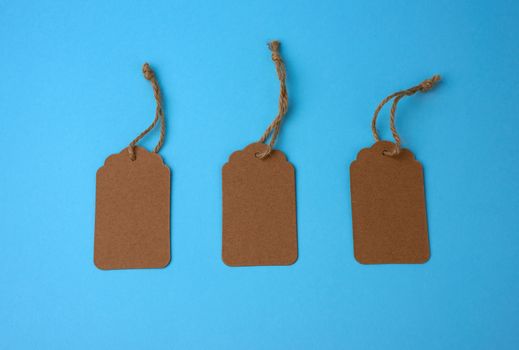 Empty brown paper tags tied with white string. Price tag, gift tag, sale tag  on the blue background, close up