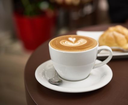 white cup with cappuccino on a brown table, selective focus