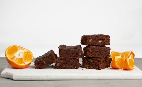 stack of square baked slices of brownie chocolate cake with walnuts on a white wooden board