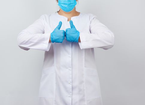 medic woman in white coat and mask, wearing blue medical latex gloves on her hands, showing like gesture in hand, approval concept