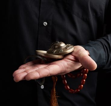 adult man in black clothes holds in his hands a pair of bronze Karatal on a leather rope, object for religious rituals, meditations and alternative medicine, low key