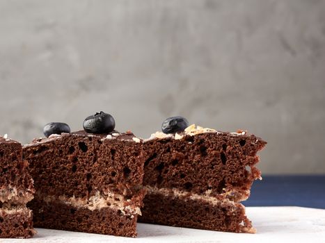 triangular pieces of chocolate biscuit cake with butter cream on a white wooden board, gray background, close up