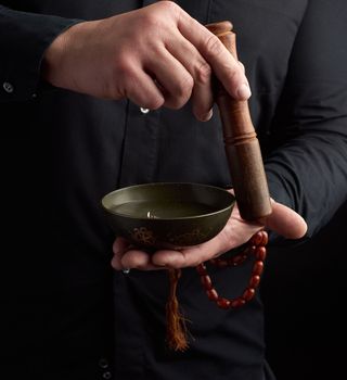 adult man in a black shirt rotates a wooden stick around a copper Tibetan bowl. ritual of meditation, prayers and immersion in a trance. Alternative treatment