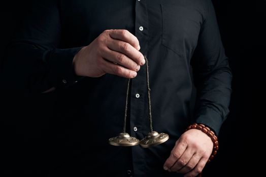adult man in black clothes holds in his hands a pair of bronze Karatal on a leather rope, object for religious rituals, meditations and alternative medicine, low key
