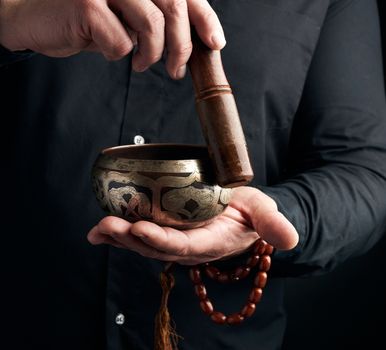 adult man in a black shirt rotates a wooden stick around a copper Tibetan bowl of water. ritual of meditation, prayers and immersion in a trance. Alternative treatment