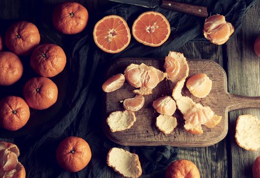 ripe round tangerines and cut in half on an old vintage cutting board. Healthy vegetarian food. Citrus fruit, top view