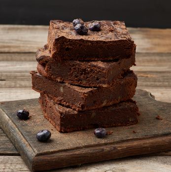 stack of square baked slices of brownie chocolate cake with walnuts on a wooden surface. Cooked homemade food. Chocolate pastry. Sweet meal, homemade dessert