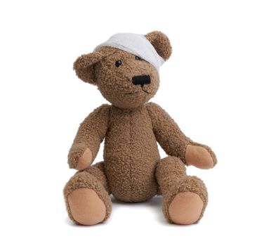 brown teddy bear with a bandaged head in a white medical bandage on a white background, concept of child trauma, headache