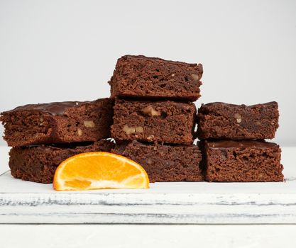 stack of square baked slices of brownie chocolate cake with walnuts on a white wooden board, close up