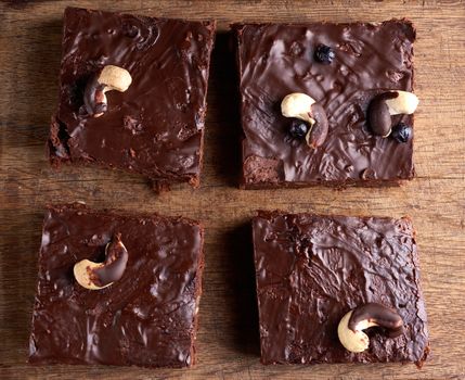 square baked slices of brownie chocolate cake with walnuts on a brown wooden surface. Cooked homemade food. Chocolate pastry. Sweet meal, homemade dessert