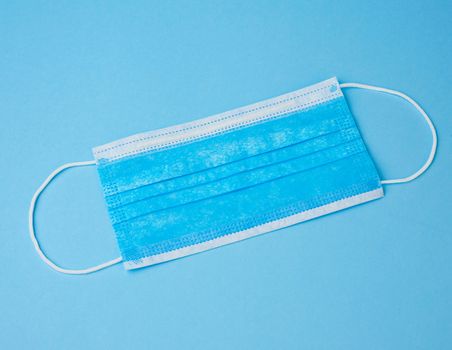 blue textile medical face mask with rubber bands from viruses and bacteria on a blue background, flat lay