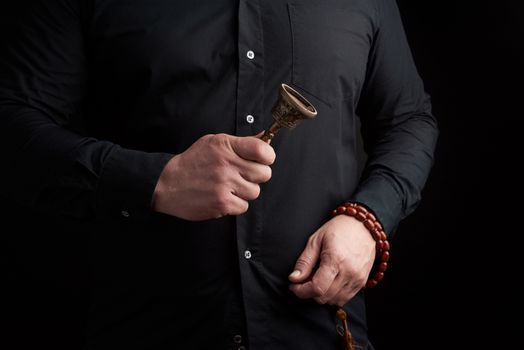 adult man in a black shirt holds a copper Tibetan ritual bell, low key. bell represents the feminine principle of excellence in wisdom.