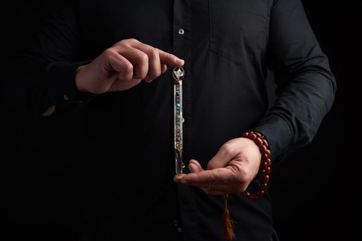 adult man in a black shirt holds a crystal chakra rod inlaid with semiprecious stones. Wand to strengthen energy and alternative medicine