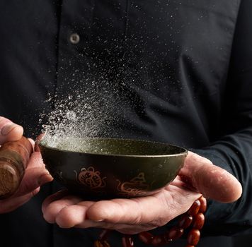 adult man in a black shirt rotates a wooden stick around a copper Tibetan bowl. ritual of meditation, prayers and immersion in a trance. Alternative treatment