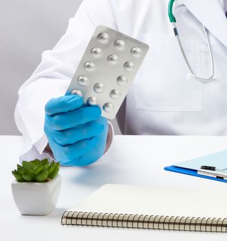 male hand with blue sterile gloves holds a stack of pills in a blister, concept for drug treatment of diseases