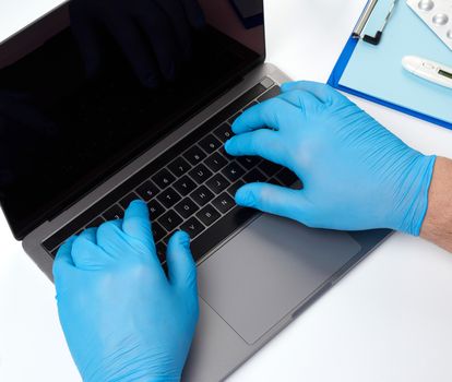 specialist doctor in blue latex medical gloves working on a laptop, concept of remote maintenance, therapist's workplace