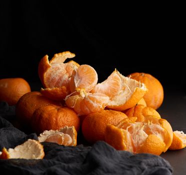 heap of unpeeled round ripe orange mandarin on a gray linen napkin, wooden table, low key