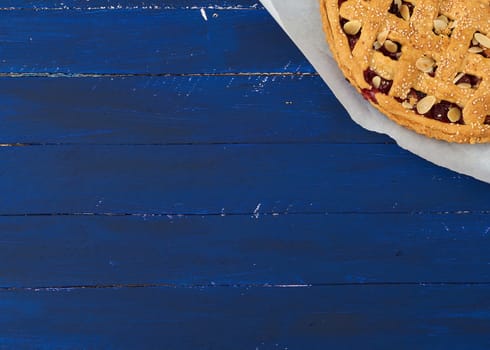 triangular slice of baked cherry pie on a white paper, blue wooden background 