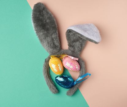 multicolored decorative Easter eggs decorated with sequins and rabbit mask on the head with ears on a green background, festive backdrop, top view