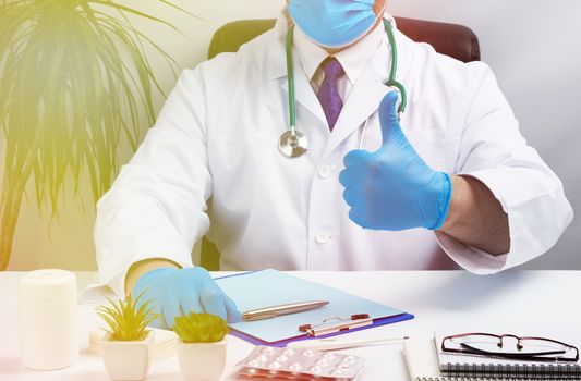 male doctor in a white coat and blue latex gloves sits at a white desk in his office and shows gesture like, medical office