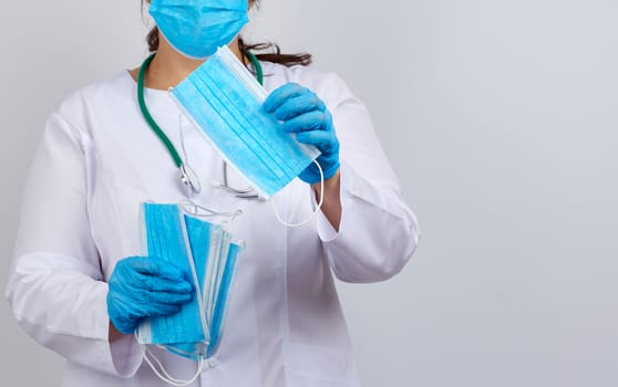 doctor in a white coat and mask holds a stack of protective face masks about the virus, doctor stands on a white background, copy space