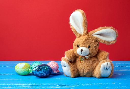 cute rabbit toy and decorative Easter eggs with sequins on a red background, festive backdrop