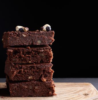 stack of square baked slices of brownie chocolate cake with walnuts on a wooden surface. Cooked homemade food. Chocolate pastry. Sweet meal, homemade dessert