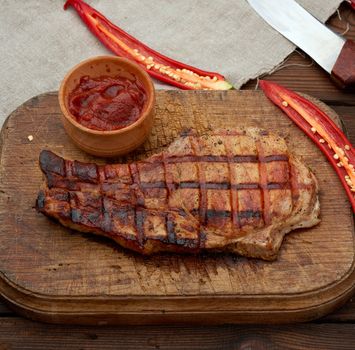 pork fried steak on the rib lies on a vintage brown wooden board, next to fresh red chili peppers, top view