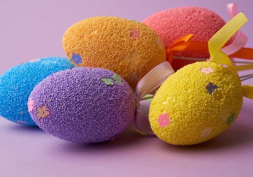multi-colored decorative Easter eggs on sticks on a purple background, festive backdrop, close up