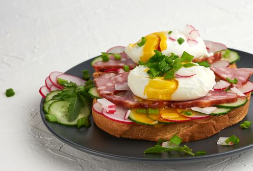 sandwich on toasted white slice of bread with poached eggs, green leaves of arugula, cucumber and radish, morning breakfast on a round plate, white background, eggs benedict 