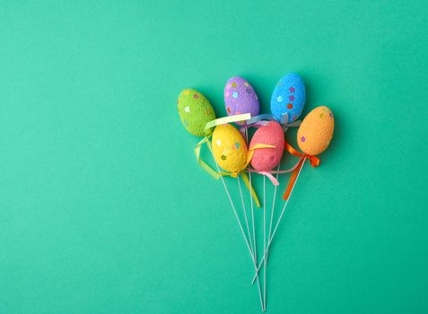 multi-colored decorative Easter eggs on sticks on a green background, festive backdrop, top view, copy space